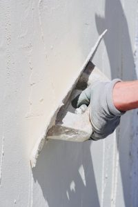 Man at work put mortar on top mesh to plaster interior construction site wall with protective gloves, blank space on wall.